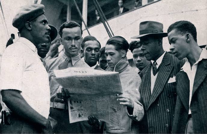 A group reading a newspaper together on the deck of a ship bound for Britain